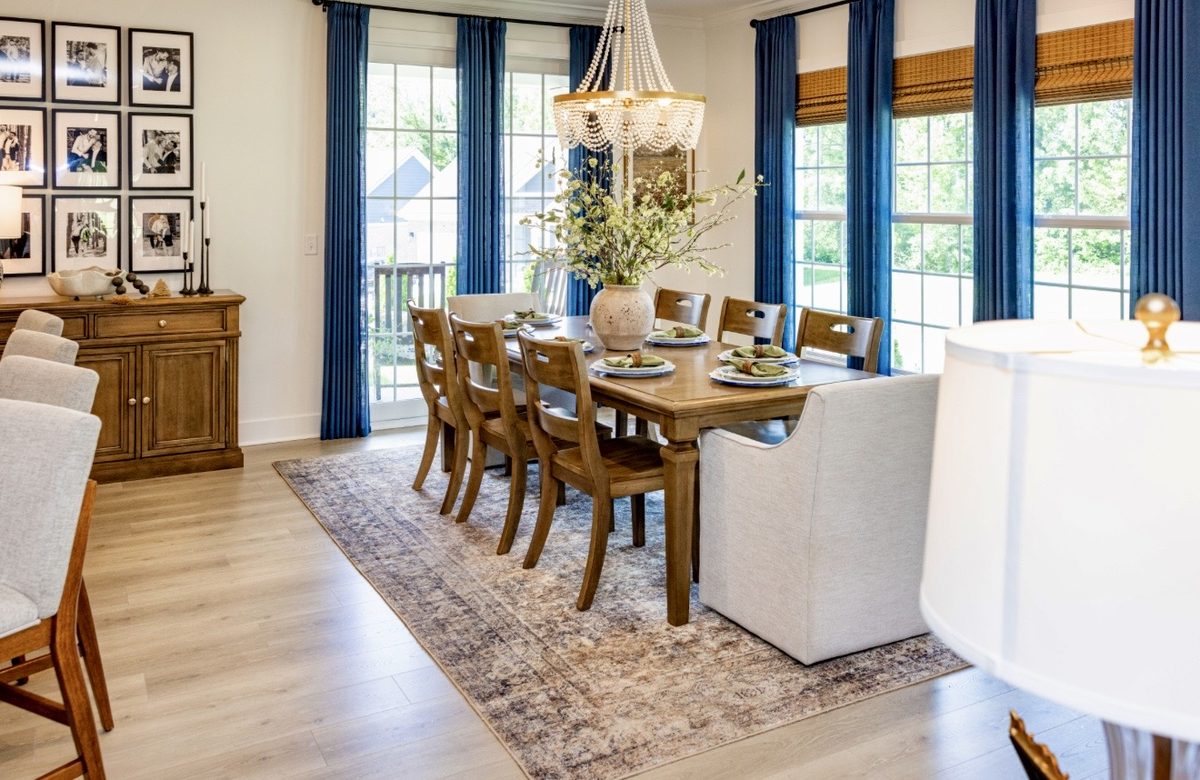 Long dining table beneath a framed gallery wall with blue drapery