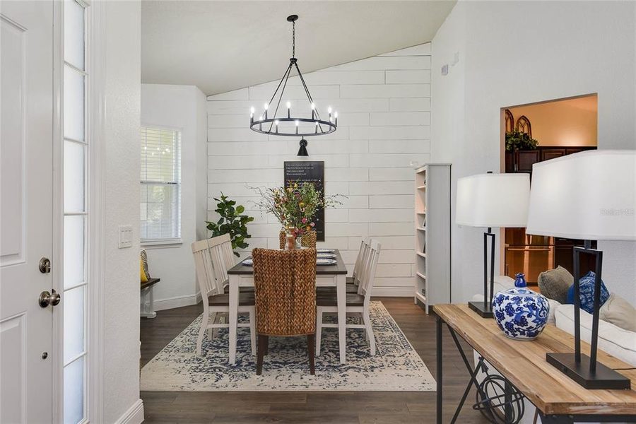 Dining room with a black iron chandelier, shiplap wall and woven runner