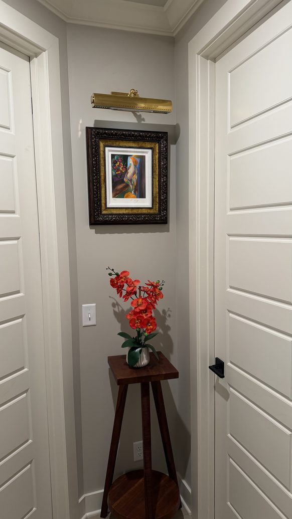Hallway nook with a brass picture light, framed print, walnut console and orchid