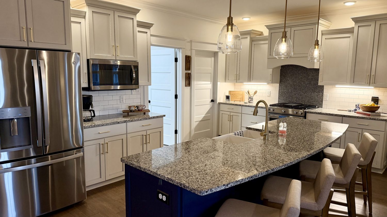 Kitchen with a navy island, granite countertops and upholstered counter stools