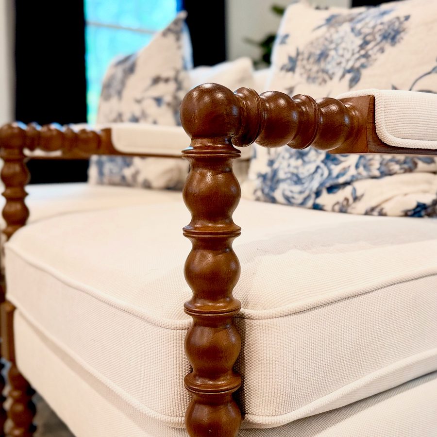 Detail of a turned spool armchair in cream linen with blue and white toile pillows