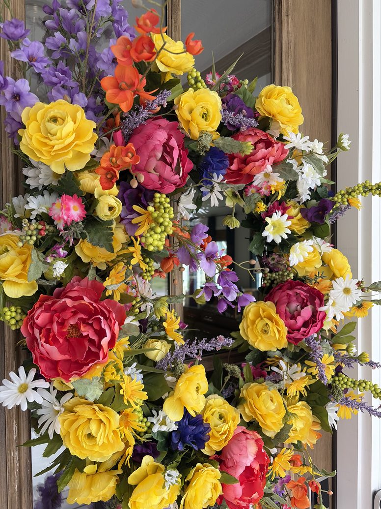 Spring wreath of peonies, ranunculus, daisies and delphinium on a wood door