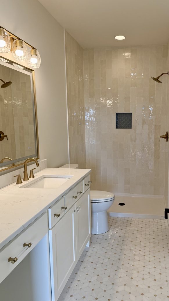 Primary bathroom with a double vanity, brass sconces and a glass shower