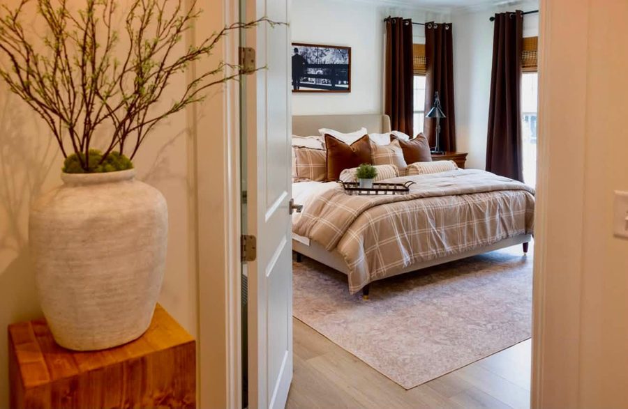 Primary bedroom seen through a doorway, layered bedding in warm neutrals