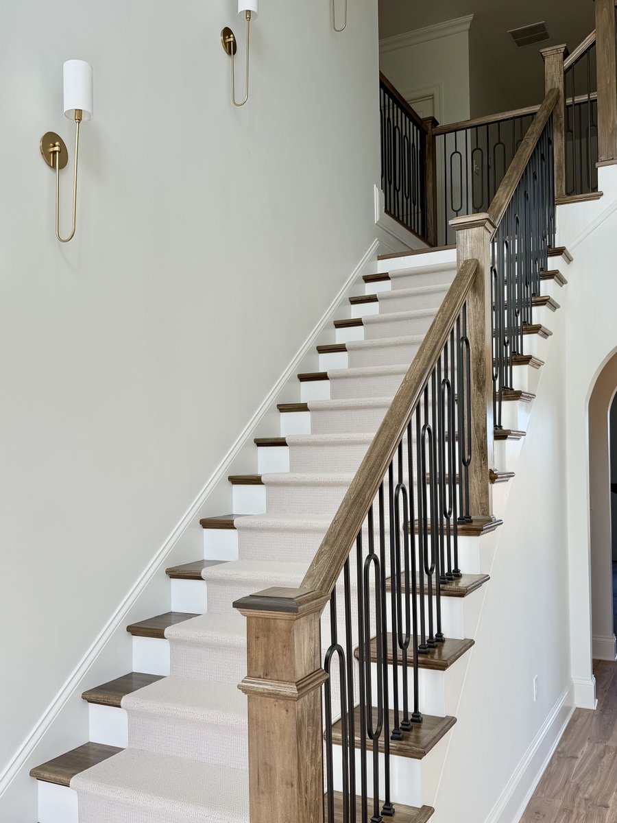 Staircase with a wood handrail, iron balusters, a wool runner and brass wall sconces